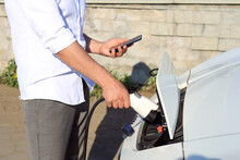 A Man With A Phone In His Hands Connects An Electric Car To The Charger