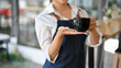 © bongkarn - Cropped image, Female barista holding a black cup of coffee