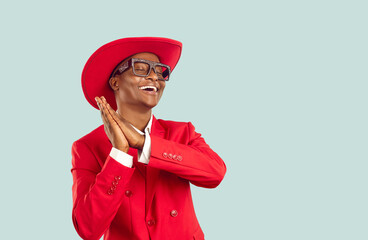 Wall Mural - Funny African man in trendy outfit dancing in studio. Happy young Tanzanian guy wearing funky red suit, hat and disco party glasses dancing isolated on blue copy space background. Fashion concept