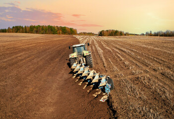 Wall Mural - Tractor with plow on field cultivating. Green tractor plowing field on sunset. Cultivated land and soil tillage. Agricultural tractor on field cultivation. Tractor disk harrow on plowing, aerial view.