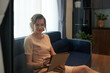 © DragonImages - Smiling businesswoman working from home, she is sitting on sofa and checking report on digital tablet