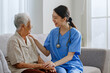 © Nattakorn - Young Asian woman nurse, caregiver, carer of nursing home cheer up a senior Asian woman at home