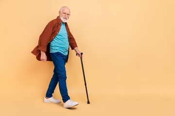 Wall Mural - Full body photo of good mood pensioner man go on walk take care of his health isolated on beige color background