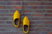 Traditional Yellow Wooden Shoes Or Clog On Red Brown Brick Wall As Background In Farmhouse, Old Pair Of Vintage And Classic Wooden Shoes, Typical Rural Countryside Villages In Netherlands.