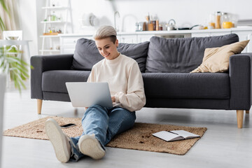 Wall Mural - full length of woman with laptop sitting on floor near couch, notebook and mobile phone