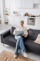 Wall Mural - high angle view of trendy woman using laptop on sofa in modern open plan kitchen