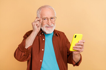 Sticker - Photo of cheerful good mood pensioner man reading book in his smartphone isolated on beige color background