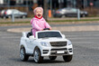 © ako-photography - little girl drives a big white childrens electric toy car in the parking lot at the residential home