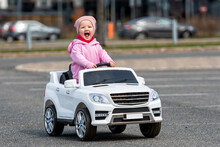 Little Girl Drives A Big White Childrens Electric Toy Car In The Parking Lot At The Residential Home