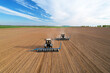 Tractor sowing seed on plowed field. Sowing seeds of corn and sunflower. Blue Tractor with disk harrow on plowing field. Seeding machinery on farm field. Seed sowing in farmland, aerial view..