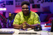 © AnnaStills - Stylish young Black man wearing neon yellow T-shirt sitting in at desk in amateur broadcasting studio