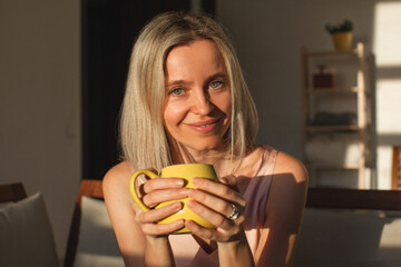 Wall Mural - Happy dreamy middle aged woman sitting on sofa in living room with cup of tea or coffee