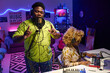 © AnnaStills - Modern gen Z African American man rapping while recording song in home studio, his girlfriend playing synthesizer and adjusting sound on mixing console