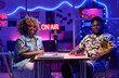 © AnnaStills - Portrait of modern young gen Z African American influencers sitting at desk in broadcasting studio at home looking at camera