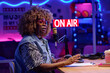 © AnnaStills - Portrait of stylish African American woman sitting at desk in podcasting or broadcasting studio speaking on topic