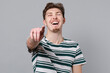 Young laughing fun cool caucasian man 20s wear blue striped t-shirt point index finger camera on you mocking joking kidding isolated on plain gray background studio portrait. People lifestyle concept.