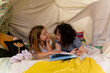 © Austockphoto - Two happy girls reading a book together in cubby house tent