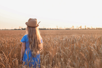 Child girl in straw hat dress in wheat field. Smiling kid in sunglasses sunset countryside. Cottagecore style aesthetic.