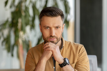 Poster - Serious Businessman Looking At Camera Sitting At Workplace In Office