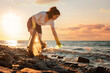 © _KUBE_ - A female volunteer is collecting plastic garbage on the seashore. Cleaning of the coastal zone. Copy space. The concept of Earth Day and environmental conservation