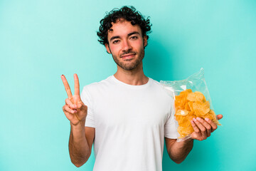 Young caucasian man holding a bag of chips isolated on blue background showing number two with fingers.