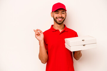 Wall Mural - Young hispanic delivery man holding pizzas isolated on white background smiling and pointing aside, showing something at blank space.