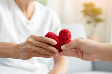 Young and senior woman holding each other hands and red yarn heart shape togetherness concept. Elderly care and protection with love from grandchild.