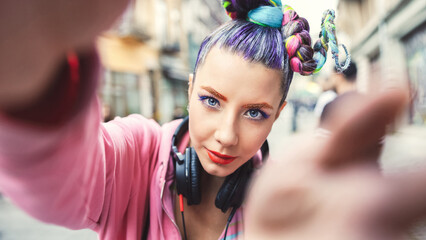 Wall Mural - Playful cool funky hipster young girl with headphones and crazy hair taking selfie on street