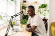 Happy young african man making audio podcast from home - Content creator recording radio show using professional microphone at small broadcast studio