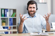 © Liubomir - Annoyed call center employee looks at the camera and quarrels with the client, the man uses a headset for a video call