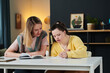© AnnaStills - Young Caucasian woman spending time with her younger sister with Down syndrome helping with homework task