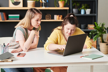 Young girl with Down syndrome using laptop searching something in Internet during individual lesson with teacher at home