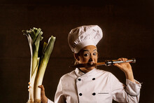Expressive Female Clown Biting Knife While Standing In Studio With Leeks In Hand
