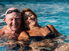 Happy Elderly Spouses Swimming In Pool On Sunny Day
