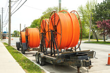Large spools of smooth walled HDPE plastic cable (orange) conduit on trailers waiting to be installed and carry utility cables for new construction.  Shot in an industrial area of Toronto in spring.