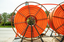 Large spools of smooth walled HDPE plastic cable (orange) conduit on trailers waiting to be installed and carry utility cables for new construction.  Shot in an industrial area of Toronto in spring.