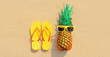 Summer vacation concept - pineapple and yellow flip flops on the beach sand background