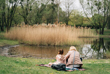 Anonymous Mother With Little Daughter Sitting At Lakeside During Picnic In Park