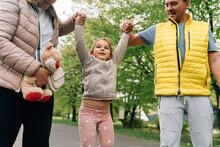 Cheerful Little Kid Holding Hands Of Grandparents In Park