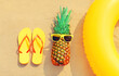 Summer vacation concept - pineapple and inflatable ring with yellow flip flops on the beach on sand background