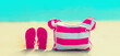 Summer vacation concept - pink bag with flip flops on beach on blue sea background