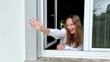 © Oleksandra - beautiful young girl teenager looks out the window and waves her hand attracting someone's attention She is dressed in a white shirt house white window white. High quality photo