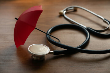 Health and insurance concept. Umbrella and stethoscope on wooden table.