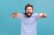 © khosrork - Portrait of happy satisfied bearded man pointing down and looking at camera, showing place for idea presentation, expressing positive emotions. Indoor studio shot isolated on blue background.