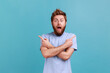 © khosrork - Portrait of astonished surprised bearded man standing with crossed hands and pointing to copy space on both sides, presenting area for promotion. . Indoor studio shot isolated on blue background.