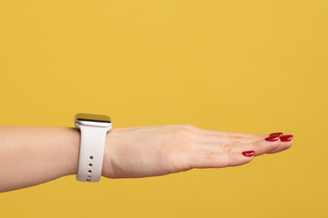 Closeup side view of woman hand with red manicure and wristtwatch with white strap, technology device. Indoor studio shot isolated on yellow background.