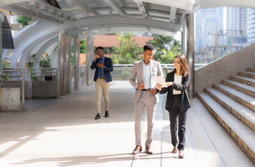 businesswoman and businessman working with tablet together outside building in city. caucasian woman and black man using tablet, executive man using mobile and calling at background