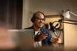 © Chanakon - Young asian man host streaming podcast with condenser microphone work on laptop at small broadcast home studio. Content creator blogger recording voice over radio interview guest conversation