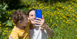 chatting with family or friends. mobile internet. Mom and preteen boy uses smartphone and taking selfies for social media sitting on the grass with dandelions on a spring day in the garden. social net