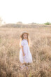 © capable97 - A cute little girl with long blond curly hair in a white summer dress and a straw boater hat in a field in the countryside in summer at sunset. Nature and Ecolife